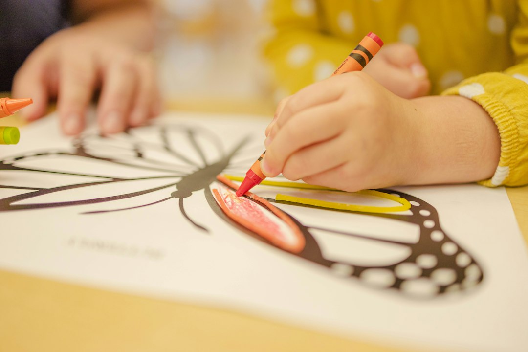 Child coloring a butterfly drawing with a red crayon