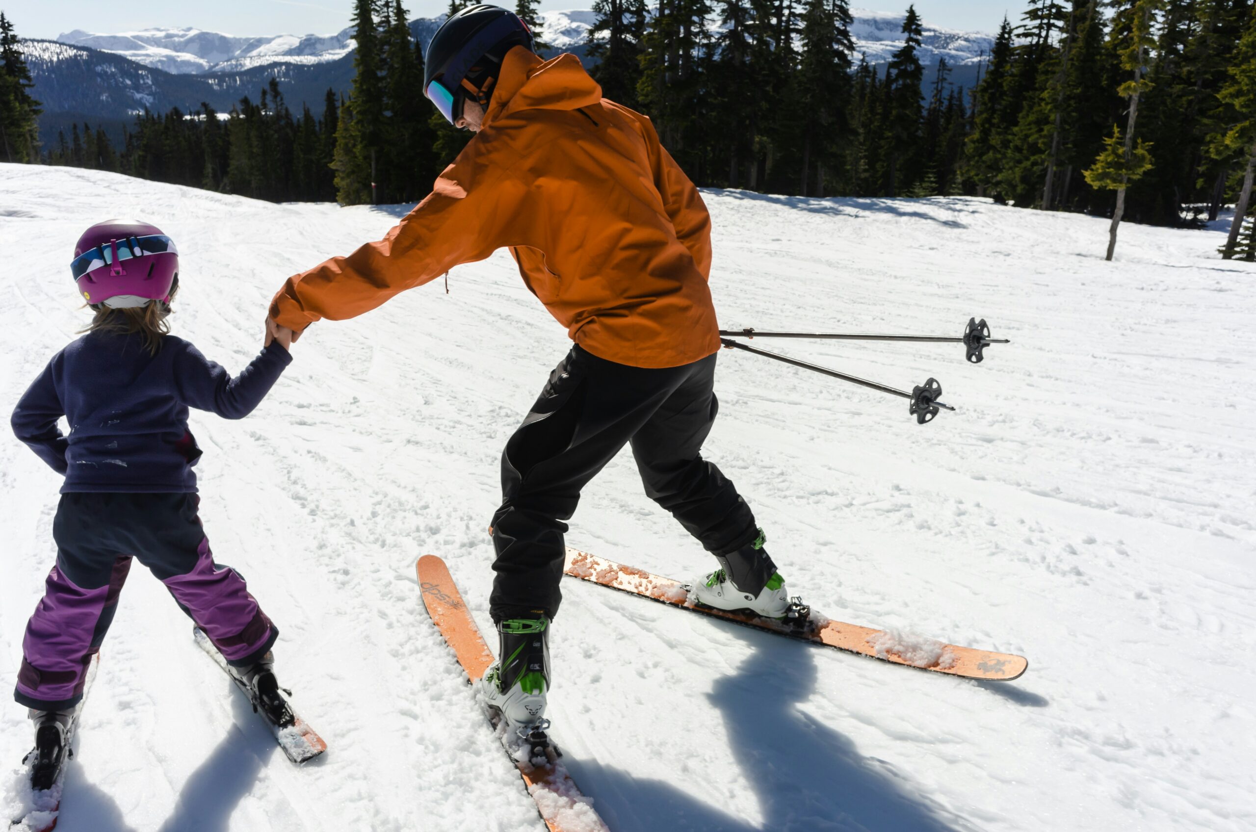 An adult instructor helping a child learn to ski on a snowy slope
