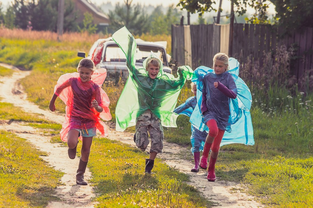 Children in colorful raincoats racing along a village path after rain