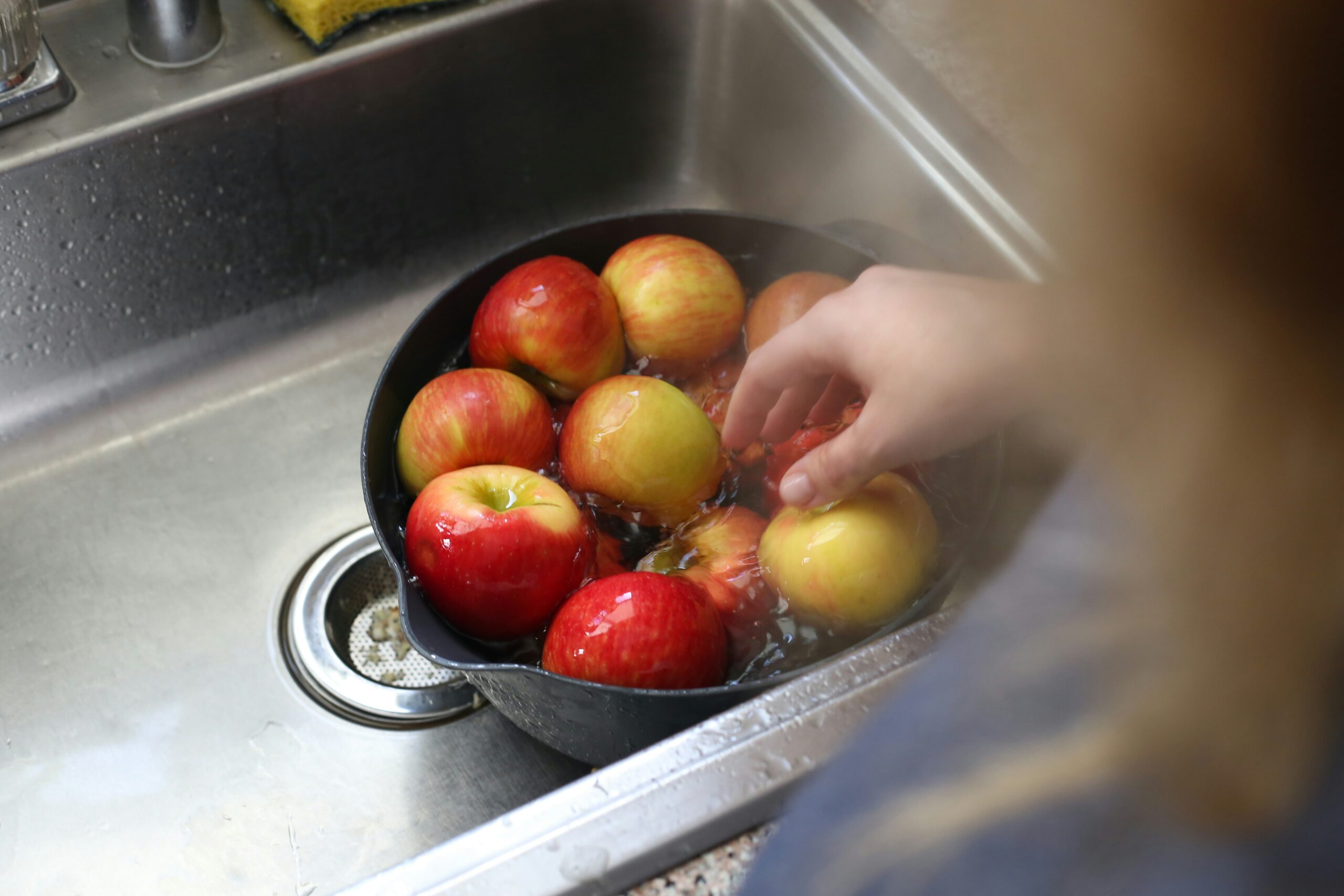Hands washing fresh produce in a sink for a supervised water sensory activity